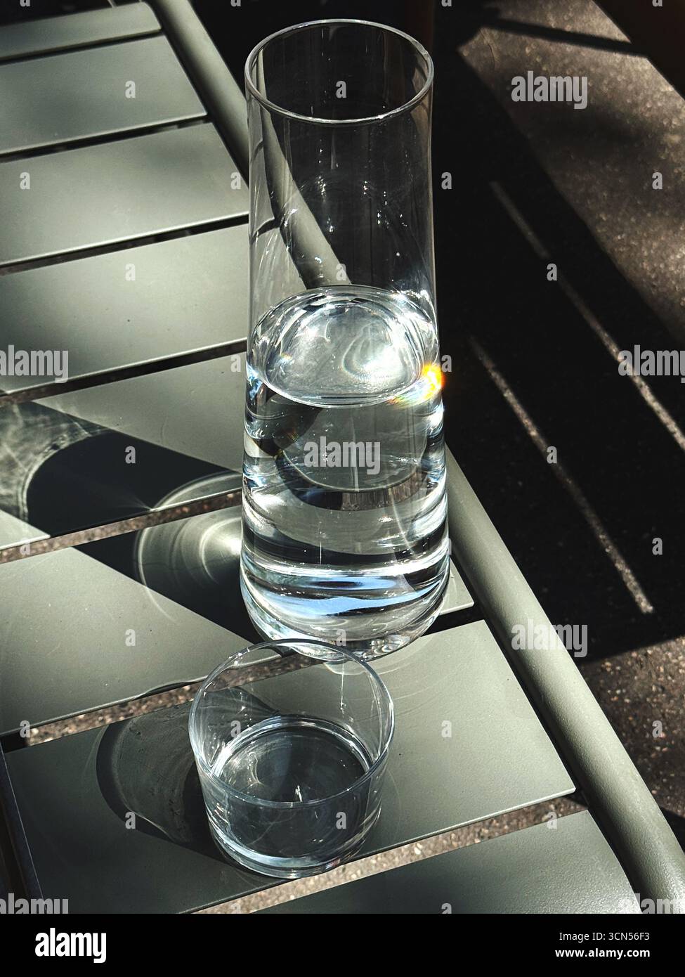 Une grande carafe en verre mince remplie d'eau se dresse sur une table de café. Un verre plus petit se trouve à côté, prêt à être rempli, soulignant un moment simple et rafraîchissant. Banque D'Images