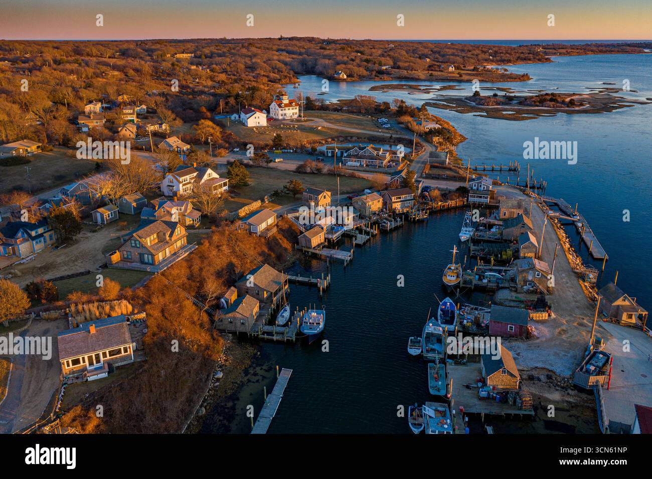 Vue aérienne de la lumière dorée baignant le pittoresque village portuaire, soulignant le contraste entre les docks rustiques et les eaux sereines de Menemsha, Martha's Vineyard, Massachusetts, États-Unis. Banque D'Images