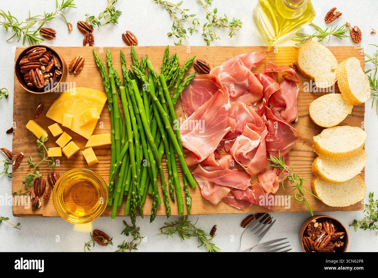 Une planche de charcuterie magnifiquement agencée avec des tranches de jambon, des blocs de fromage, des asperges fraîches et des noix croquantes. Parfait pour déguster avec frien Banque D'Images