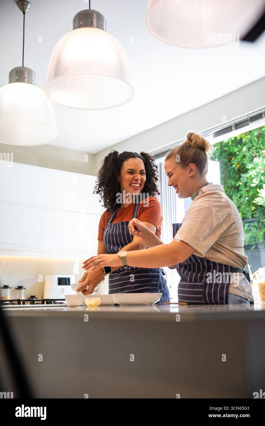 Diverses amies féminines portant des tabliers rayés remuant des œufs dans un bol à mélanger dans la cuisine Banque D'Images