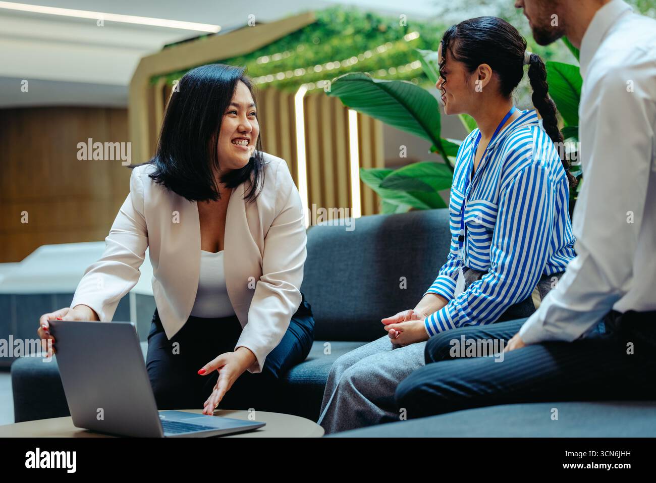 Une femme d'affaires chinoise mène énergiquement une réunion avec des collègues dans un cadre de bureau moderne. L'équipe, habillée en tenue professionnelle, est engagée Banque D'Images