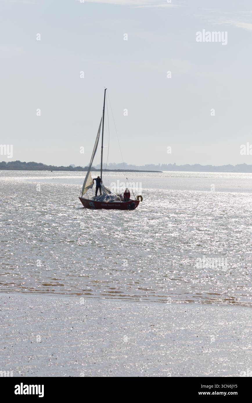 River Colne à Wivenhoe par une journée ensoleillée avec la lumière du soleil scintillant sur l'eau. Un yacht de Colne Yacht Club avec ses voiles blanches levées sur la rivière. Banque D'Images