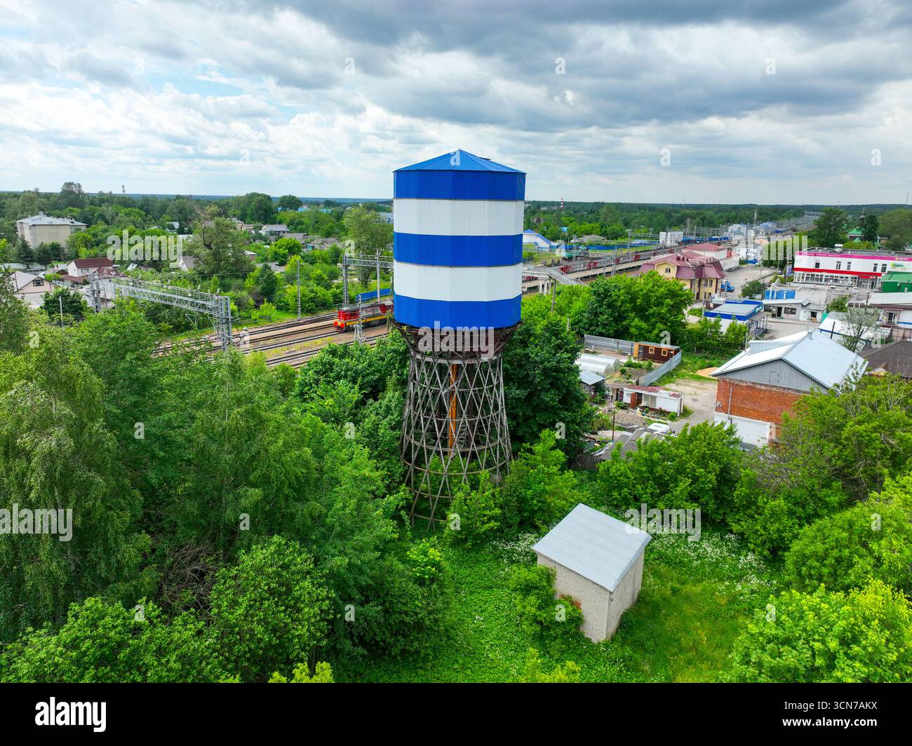 Une vue aérienne d'un château d'eau rayé bleu et blanc, à côté des voies ferrées avec un train qui passe, et des bâtiments en arrière-plan. Banque D'Images