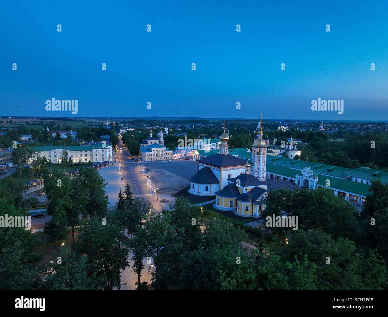 Une large vue aérienne du centre-ville de Souzdal au crépuscule, montrant une église historique et de longs bâtiments bas avec des toits verts et des dômes dorés. Banque D'Images