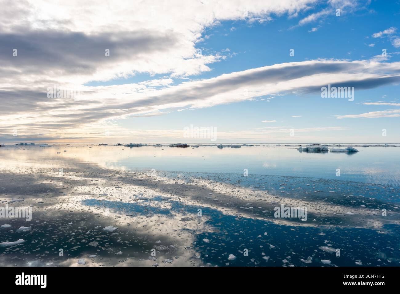 Klerckbukta Nordaustlandet Svalbard Océan Arctique Banquises flottantes | NORDAUSTLANDET, Svalbard — Des banquises flottantes dispersées dérivent sur les eaux miroitantes au large de la côte sud-est de Nordaustlandet près de Klerckbukta, reflétant un ciel de nuages superposés. La baie se trouve près de Kapp Mohn, le point le plus méridional de l'île, et fait face à la calotte glaciaire d'Austfonna, qui couvre plus des trois quarts de Nordaustlandet et reste inaccessibles aux visiteurs en dehors de la brève fonte de fin d'été. Banque D'Images