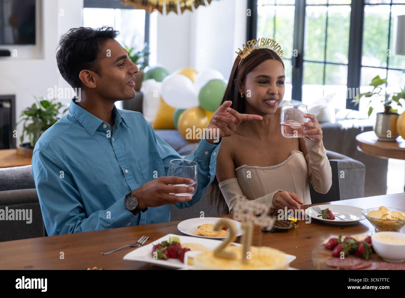 Couple indien toast anniversaire avec des verres à la table à la maison à côté du gâteau, fille dans la tiare, espace de copie Banque D'Images