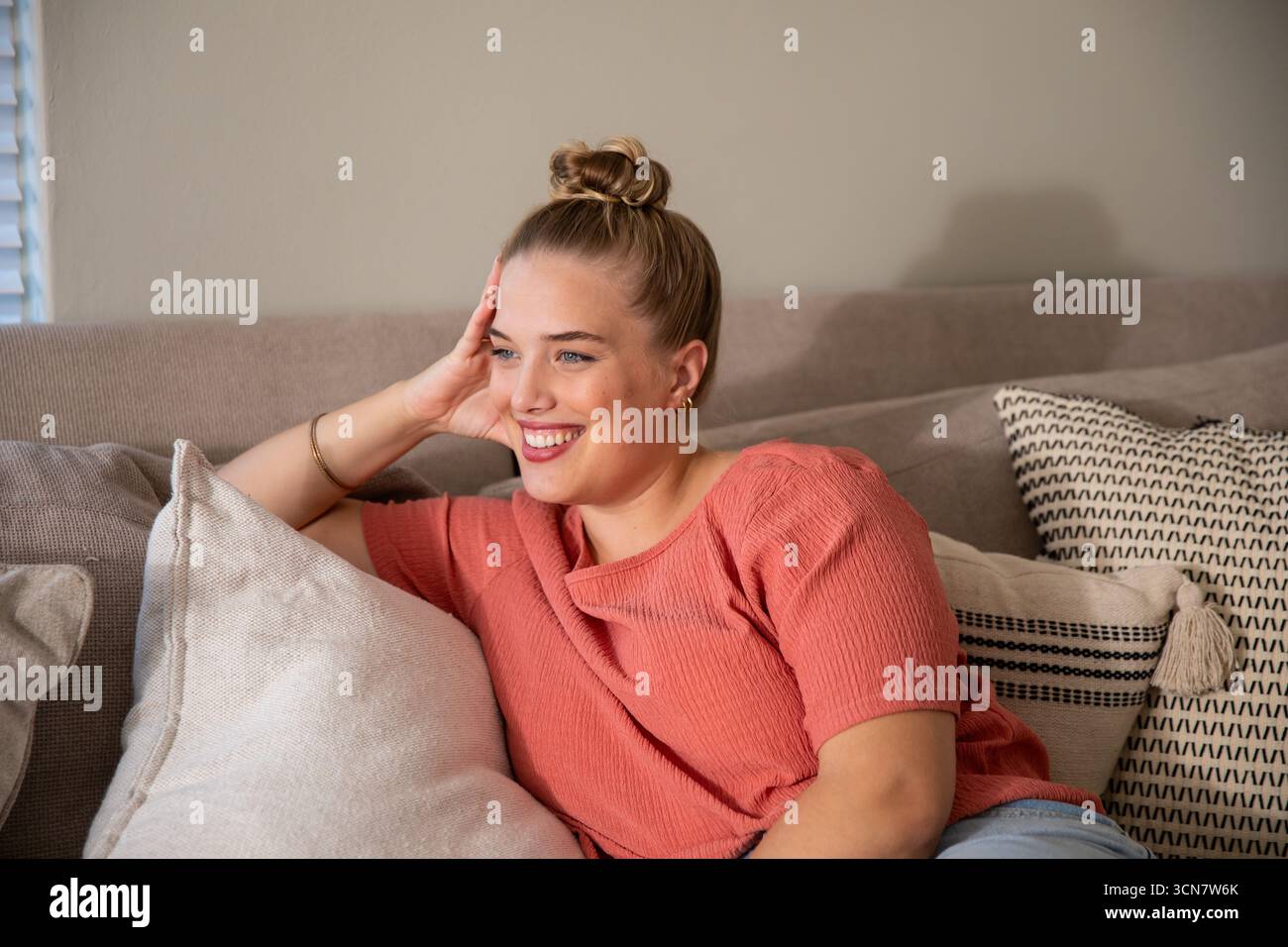 Femme allongée sur un canapé dans le salon avec des oreillers décoratifs portant un dessus de corail, un Jean denim Banque D'Images