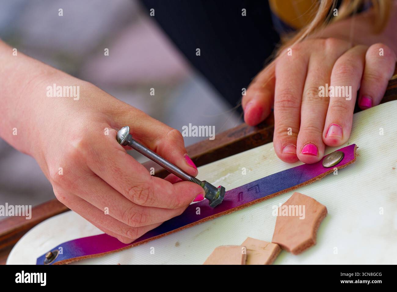 Une fille avec des ongles roses aligne un timbre sur une bande rose. Elle tape et forme un nom dans le cuir. La station soignée offre de nombreuses lettres à choisir, inviti Banque D'Images