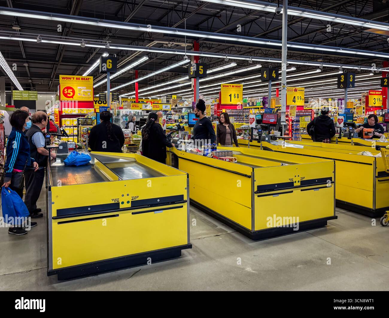 Les comptoirs-caisses des supermarchés ne sont pas superflus avec les clients et les caissiers. Les caisses jaunes, les affiches promotionnelles et un environnement de vente au détail très fréquenté illustrent un Banque D'Images