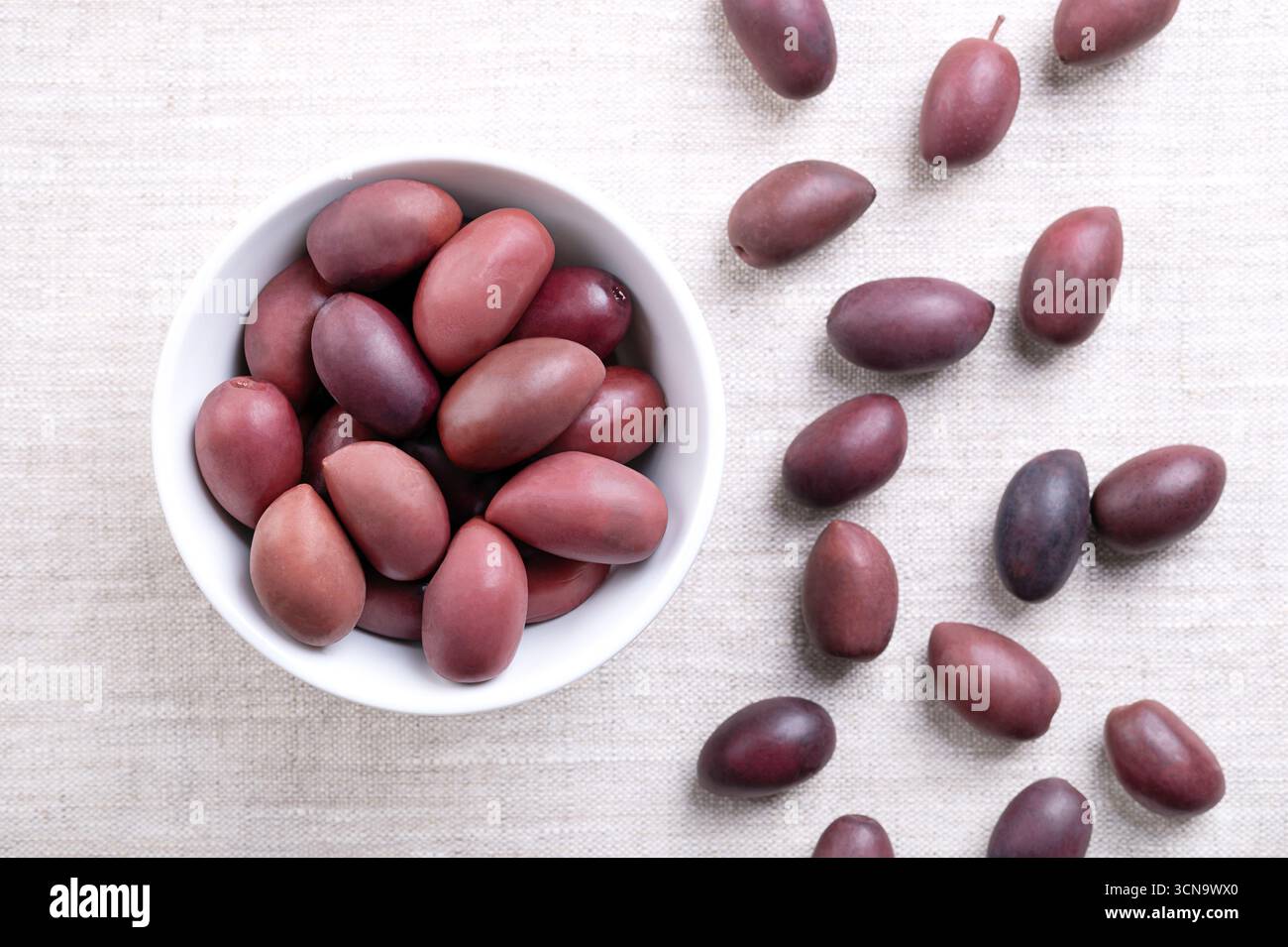 Olives Kalamata avec fosse, dans un bol blanc sur lin. Grandes olives violettes cueillies à la main, à la texture lisse et charnue, nommées d'après la ville grecque Kalamata. Banque D'Images