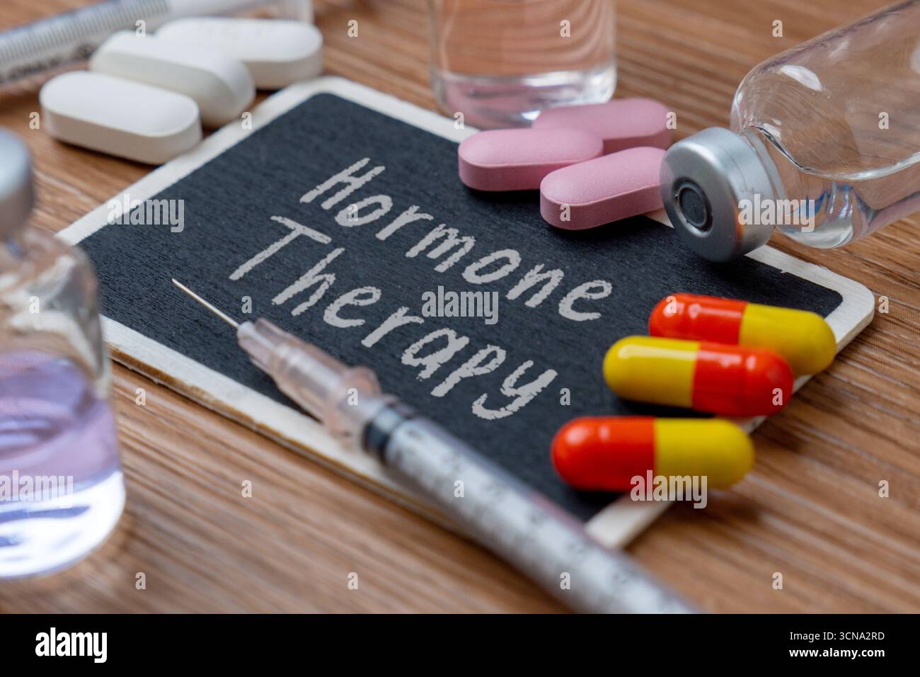 Diverses pilules, capsules et flacons avec une seringue sur une table en bois. Un petit tableau au centre porte les mots 'hormonothérapie'. Banque D'Images
