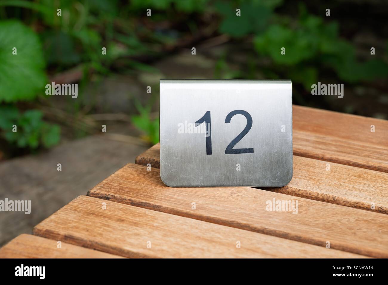 Un numéro de table '12' se trouve sur une table en bois, susceptible d'aider les clients à trouver leur place réservée dans un lieu extérieur. Banque D'Images