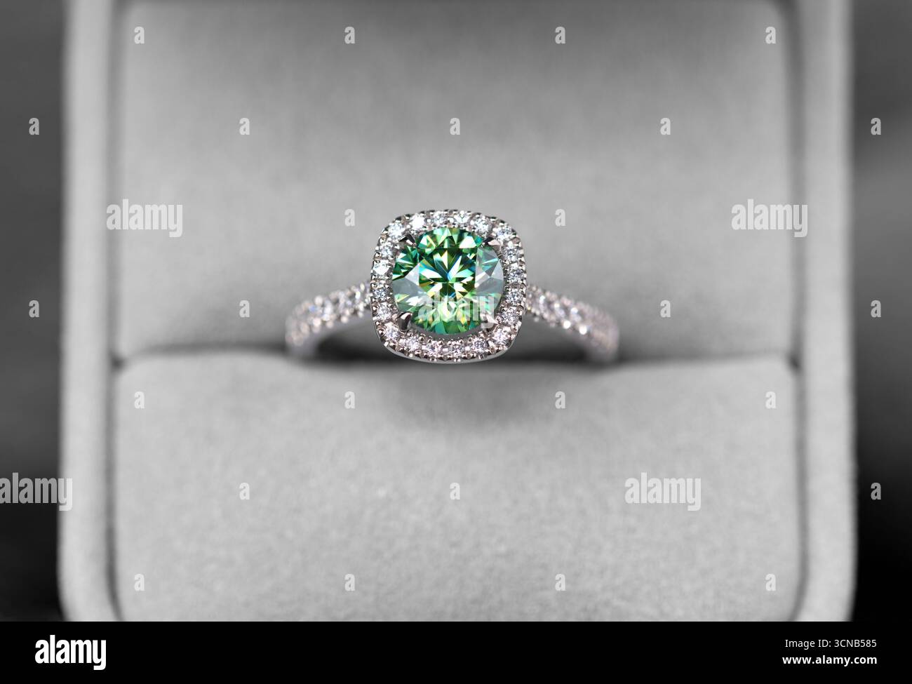 Une bague en diamant vert et blanc est affichée dans une boîte blanche. La bague est sertie dans une bande d'or et a un halo de diamants autour d'elle. L'anneau est un symbole Banque D'Images