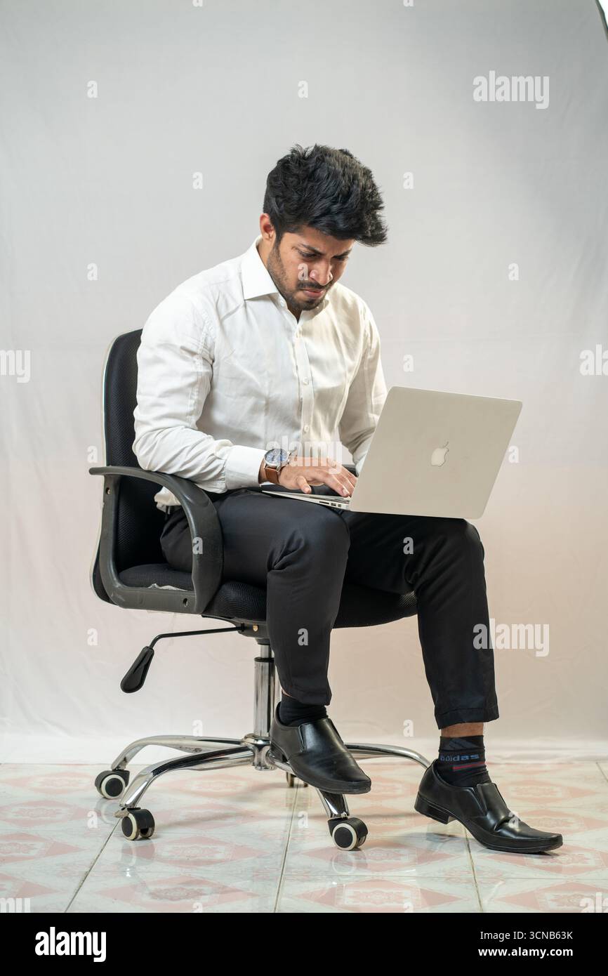Un jeune homme assis et utilisant un ordinateur portable. Banque D'Images