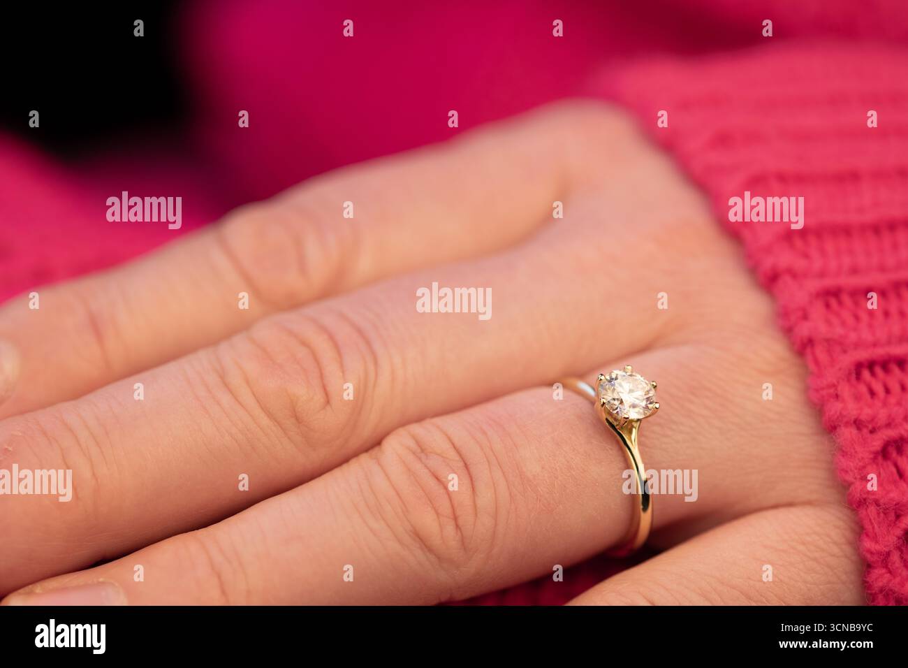 La main d'une femme tient une bague avec un diamant dedans. La bague est en or et la femme porte un pull rose Banque D'Images