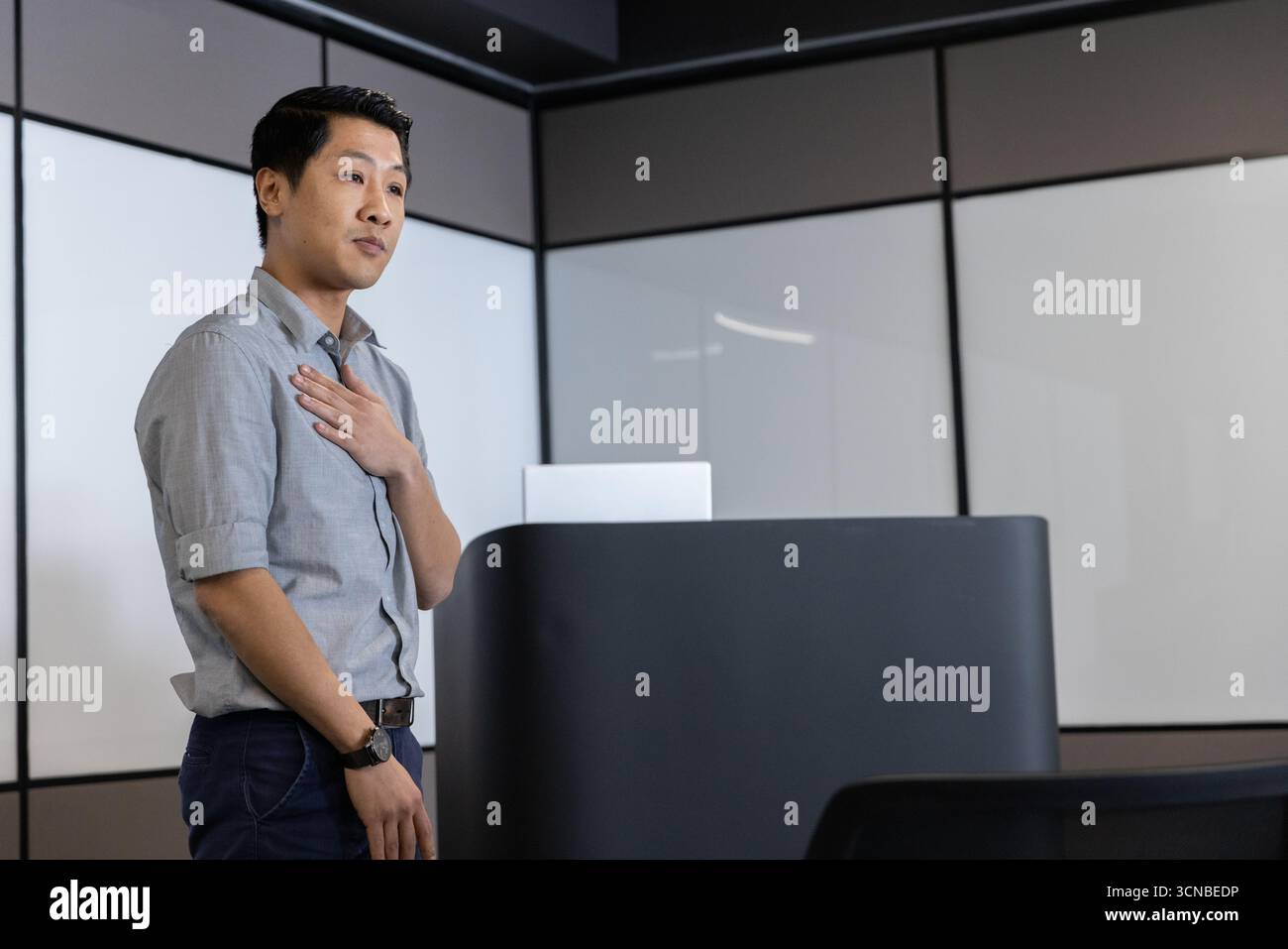 Homme asiatique mi-adulte présentant à côté du podium dans la salle de réunion, soulignant le point, vérifiant l'ordinateur portable Banque D'Images