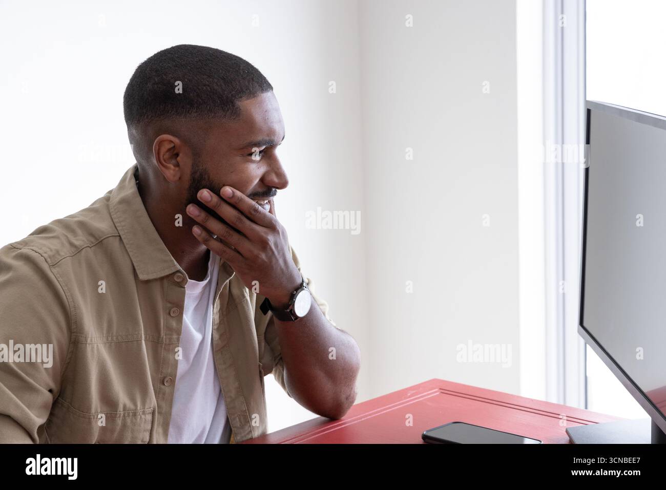 Homme afro-américain assis au bureau dans le bureau à domicile à l'aide d'un moniteur d'ordinateur et d'un smartphone Banque D'Images