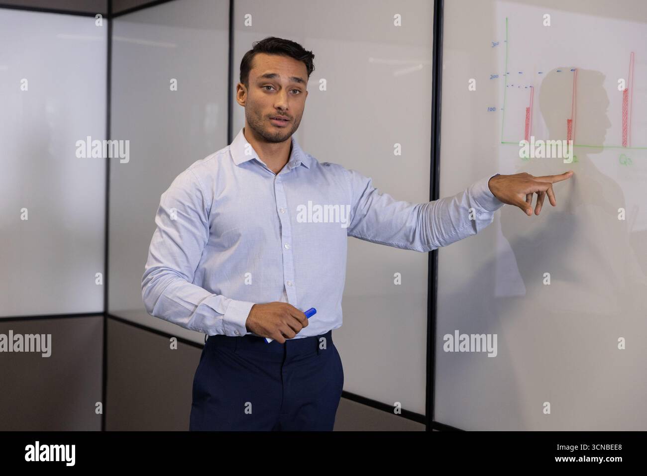 Homme debout à côté du tableau blanc pointant vers le graphique à barres avec un bouchon marqueur bleu dans la salle de réunion Banque D'Images