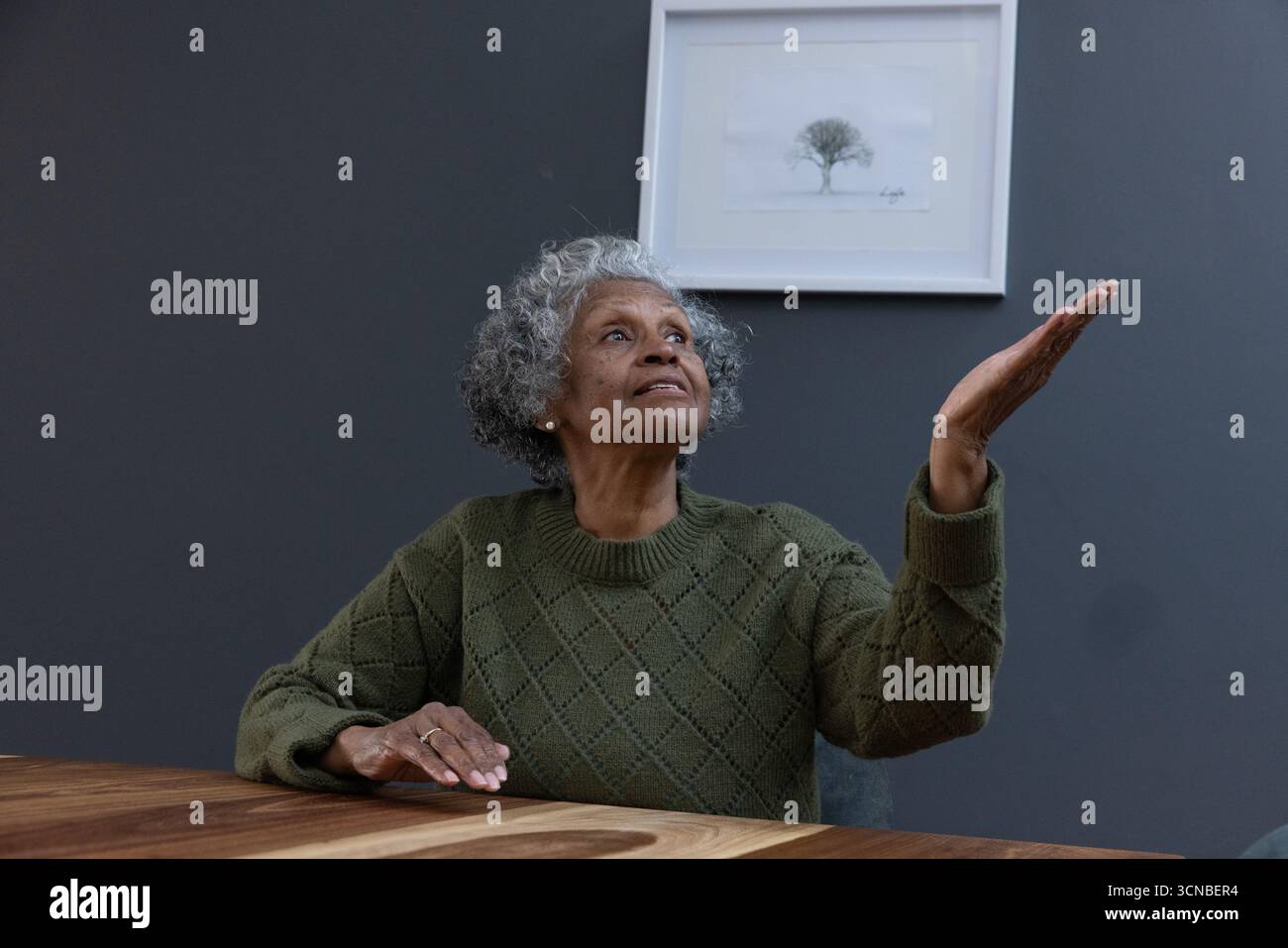 Femme afro-américaine senior portant un pull à la table de la cuisine soulevant le palmier sous l'impression d'arbre Banque D'Images