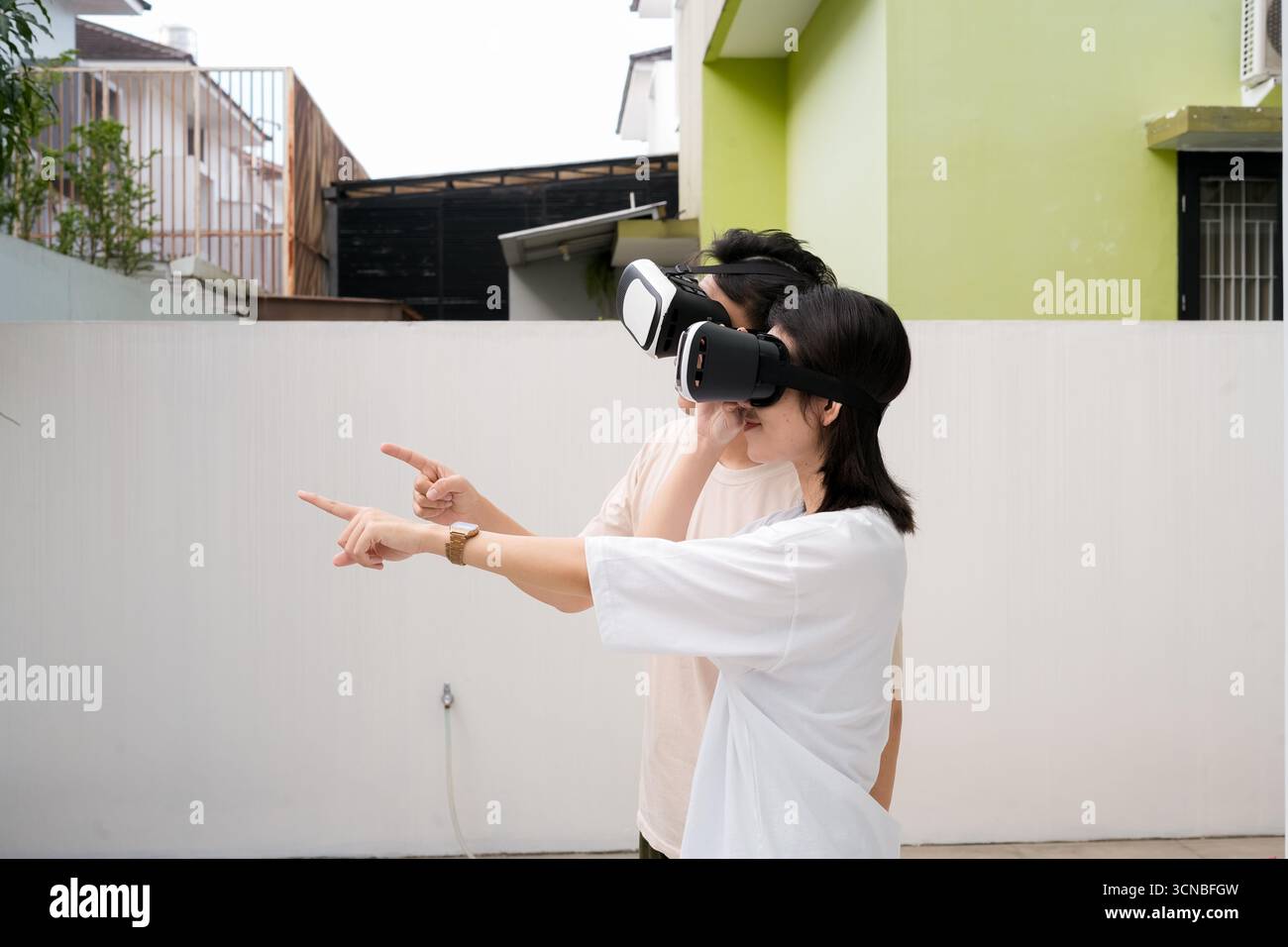 Les couples portent des casques VR dans une arrière-cour urbaine ensoleillée, explorant ensemble des visuels immersifs Banque D'Images