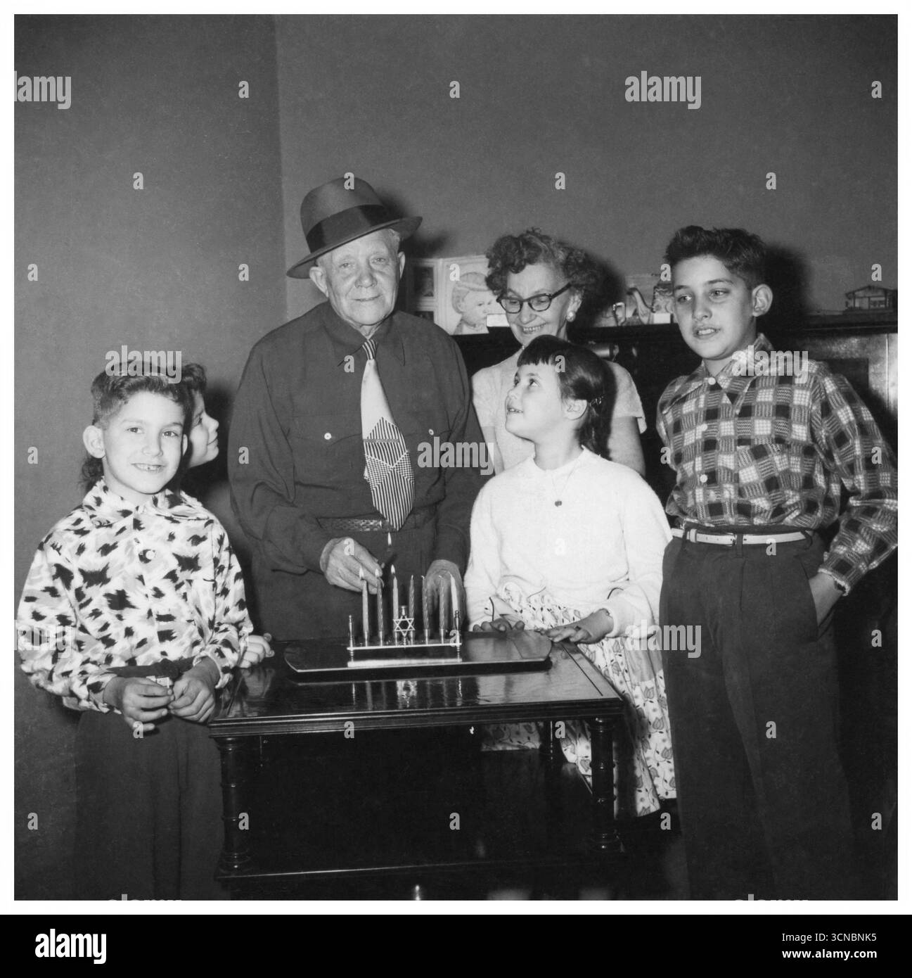 Petits-enfants avec leurs grands-parents allumant la menorah Hanukkah, 1955, décembre. Banque D'Images