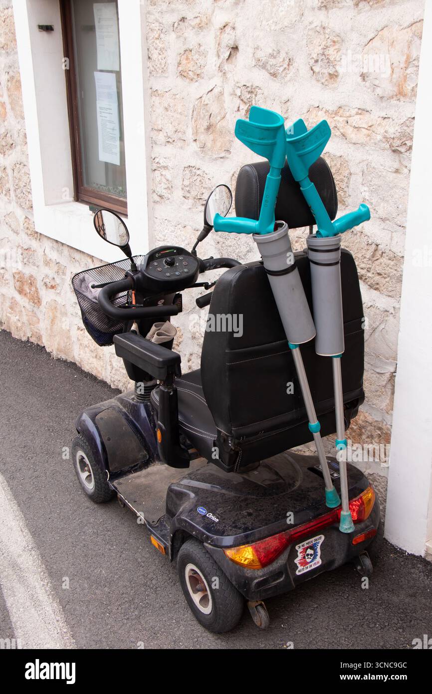 Vodice, Croatie - 7 septembre 2025 : scooter sénior de mobilité à quatre roues avec une paire de béquilles garé dans la rue Banque D'Images