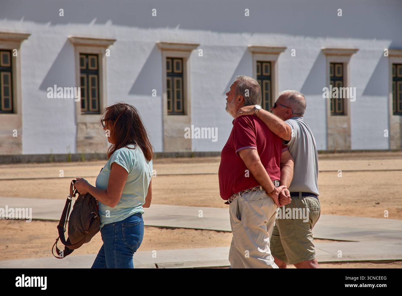 Trois retraités, deux hommes et une femme, marchent ensemble dans un cadre extérieur rappelant Alcobaca, Portugal, avec une architecture traditionnelle Banque D'Images