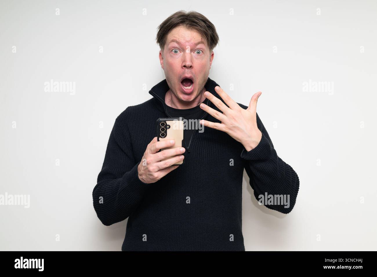 Portrait de studio de l'homme moyen adulte scandinave à l'aide du téléphone sur fond blanc regardant choqué Banque D'Images