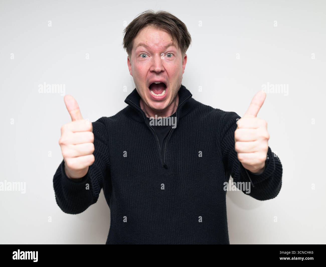 Homme scandinave mi-adulte souriant dans le portrait de pull noir sur fond blanc de studio donnant le pouce vers le haut geste Banque D'Images