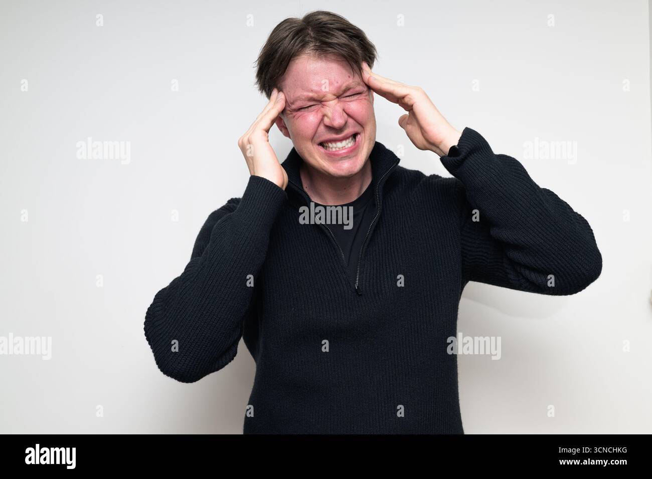 Homme scandinave mi-adulte ayant mal à la tête dans le portrait de pull noir sur fond blanc de studio Banque D'Images