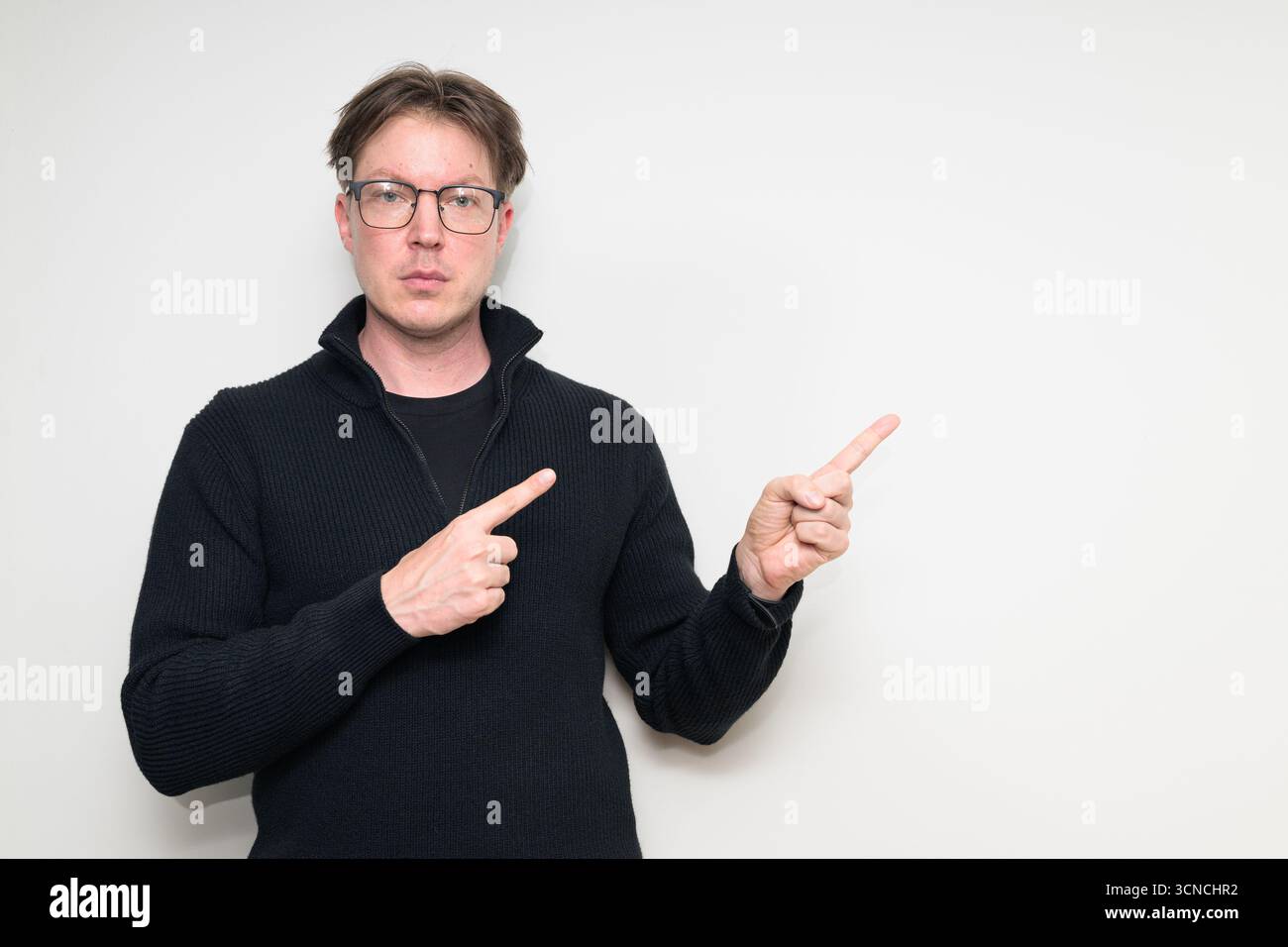 Homme adulte moyen scandinave en portrait de pull noir sur fond blanc de studio pointant le doigt pour copier l'espace Banque D'Images