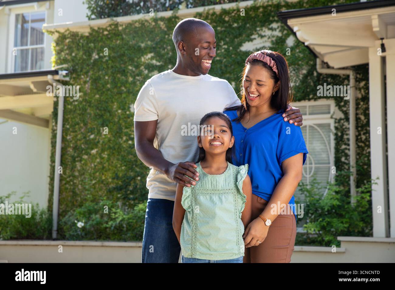 Famille diverse debout sur les marches du porche à la maison de banlieue montrant lierre, arbustes Banque D'Images