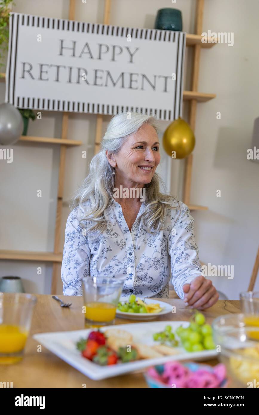 Femme assise à la table à manger pendant la partie de retraite, souriant au signe de retraite heureuse Banque D'Images