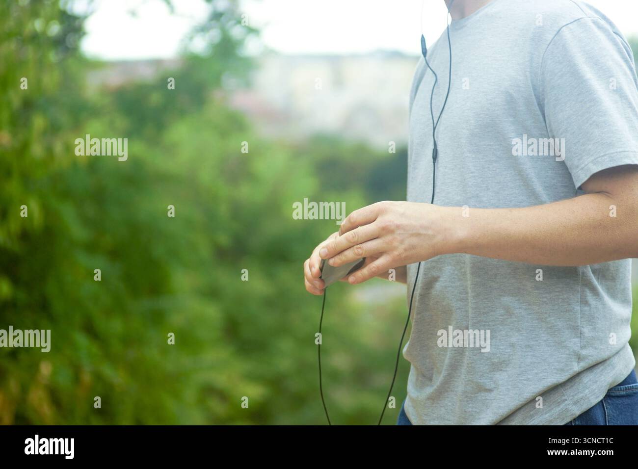 Personne tenant un téléphone portable avec casque filaire en marchant à l'extérieur. Concept de connexion numérique et de présence en ligne. Habitudes de la génération moderne Banque D'Images