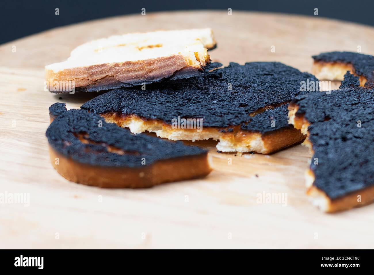 Tranche de pain grillé brûlé avec surface noire sur une planche de bois gros plan. Concept d'échec de cuisson, aliments trop cuits, mauvaise alimentation et accident de cuisine Banque D'Images