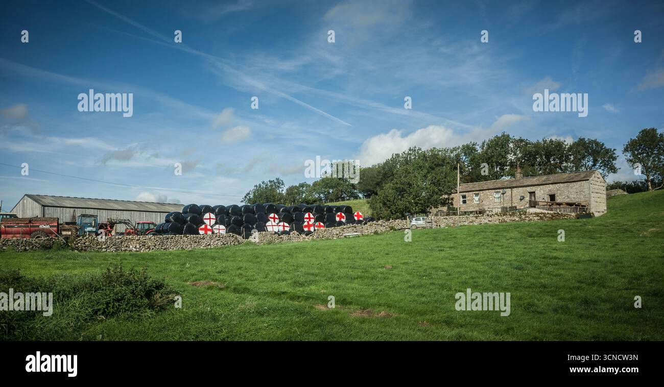 Une ferme traditionnelle en pierre dans les Yorkshire dales avec la croix anglaise de George peinte sur des balles en plastique noir, une protestation contre le gouvernement Banque D'Images