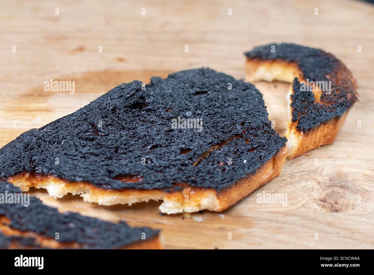 Tranche de pain grillé brûlé avec surface noire sur une planche de bois gros plan. Concept d'échec de cuisson, aliments trop cuits, mauvaise alimentation et accident de cuisine Banque D'Images