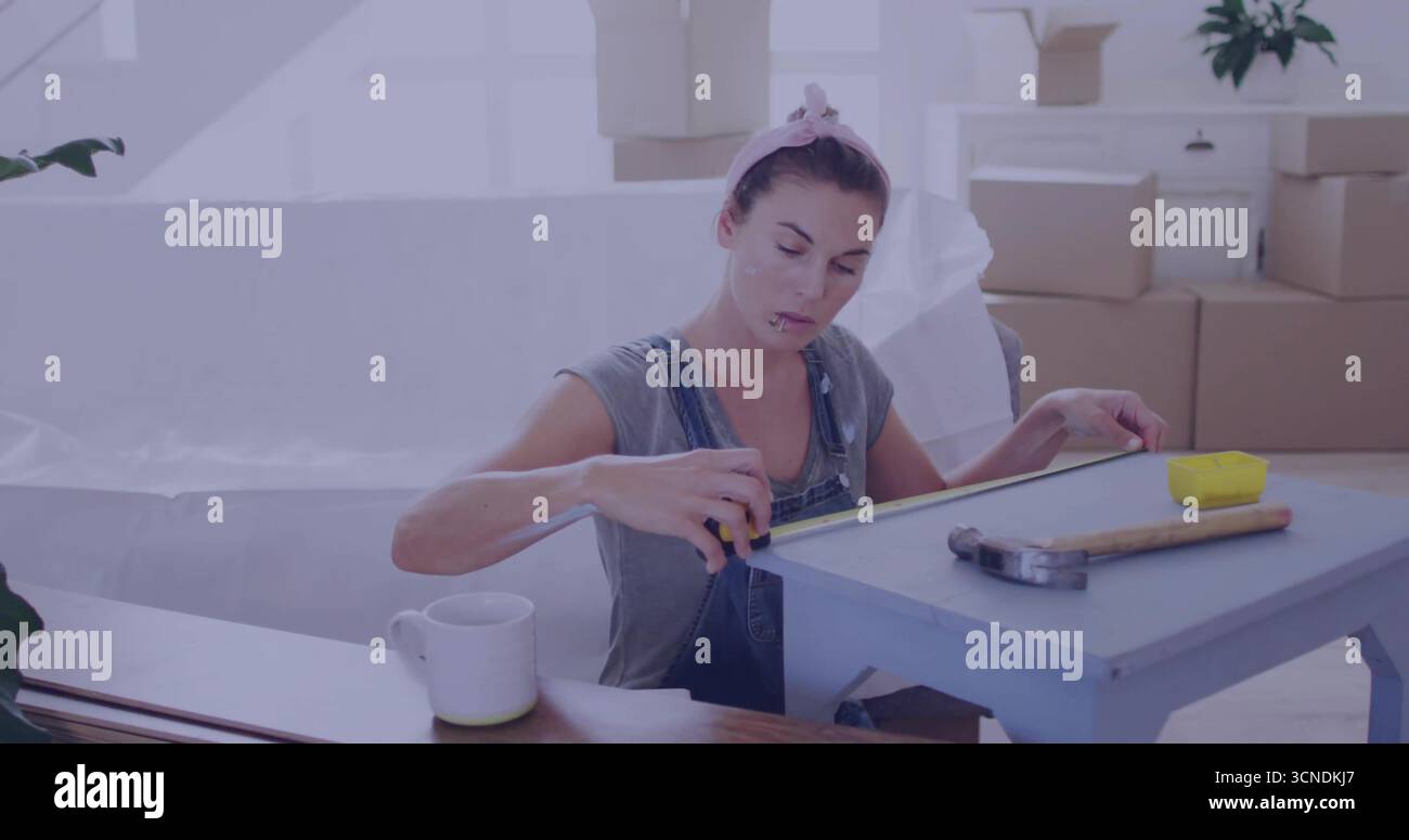Femme en salopette en denim mesurant petite table bleue dans la salle de rénovation, avec ruban à mesurer jaune Banque D'Images