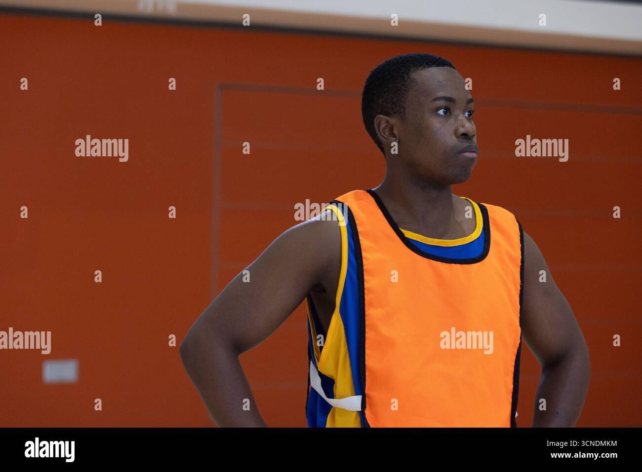 Homme afro-américain regardant droit dans le terrain de gymnastique portant un bavoir orange sur le maillot par le mur rembourré Banque D'Images