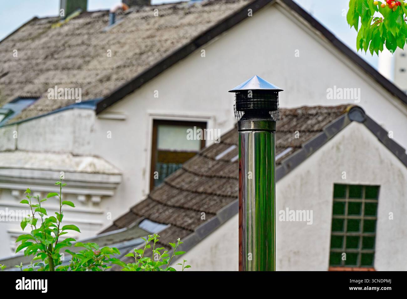 Un tuyau de cheminée en métal poli monte avec un bouchon annulaire et une maille. La suie assombrit le bord intérieur tandis que les maisons blanches et les lignes de toit sont assis derrière. Le stee brillant Banque D'Images