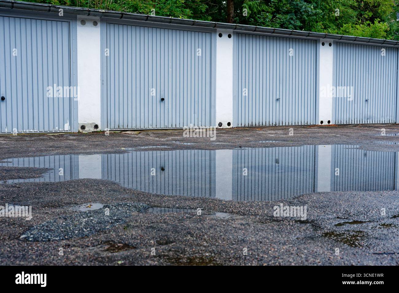 Les garages uniformes s'étendent dans le cadre, leurs panneaux pâles et propres. Un bassin peu profond dans la chaussée piège l'eau de pluie, transformant le sol en miroir Banque D'Images