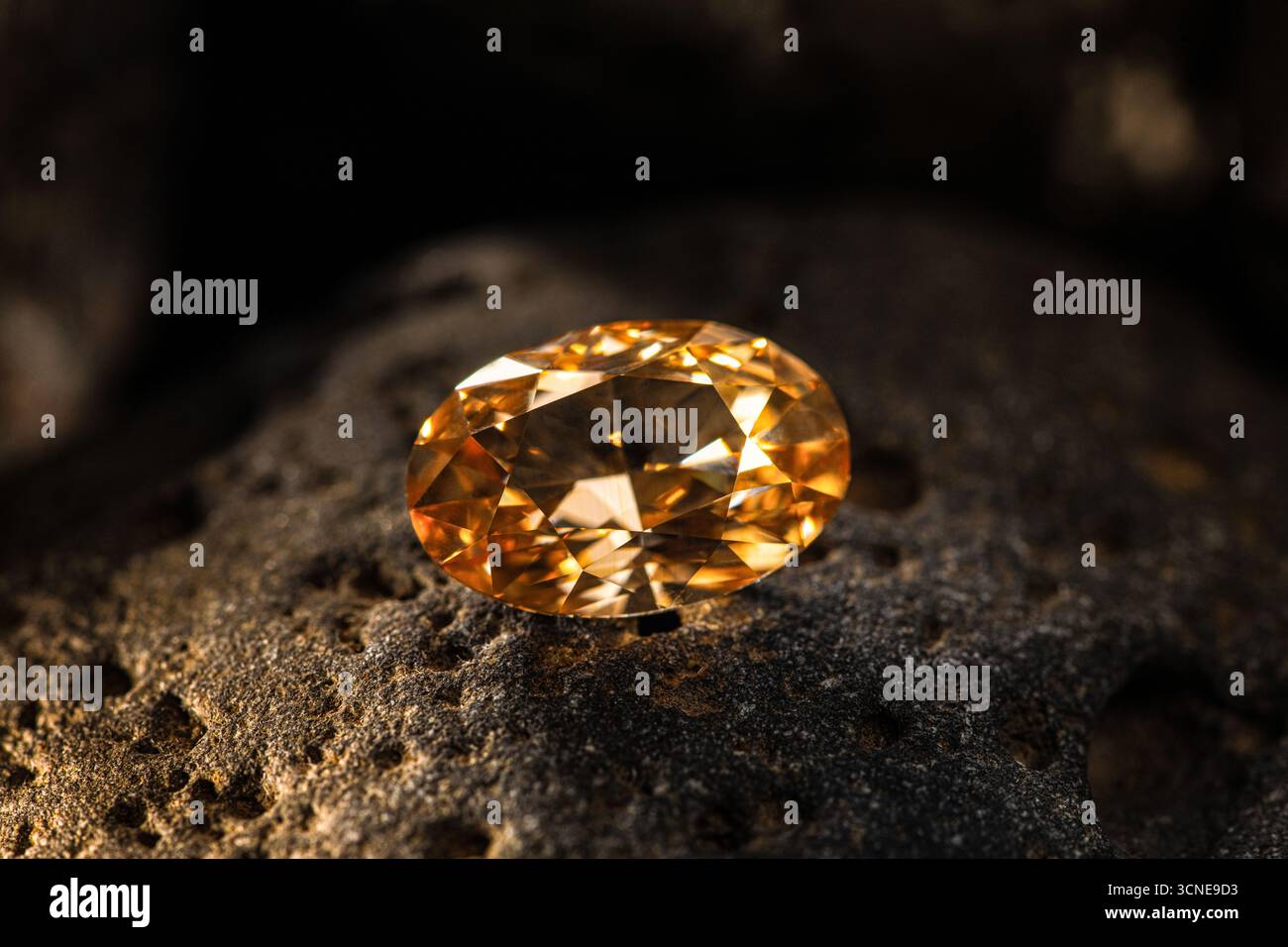 Une grande pierre précieuse orange se trouve sur un rocher. La pierre est taillée en forme de diamant et est entourée d'un fond sombre. La couleur et la forme de la pierre créa Banque D'Images