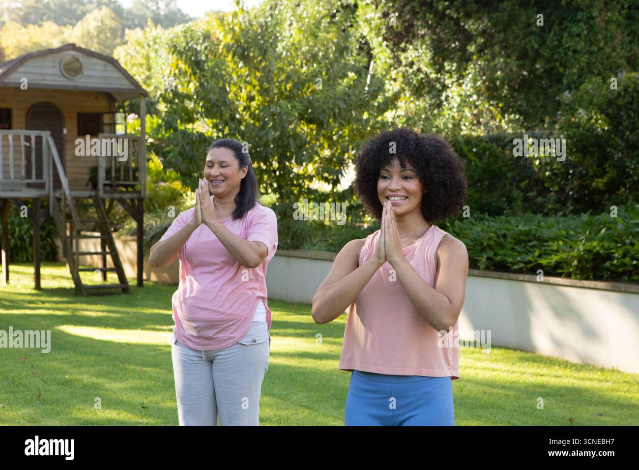 Mère hispanique et fille afro-américaine pratiquant la pose de yoga dans le jardin avec salle de jeu en bois Banque D'Images