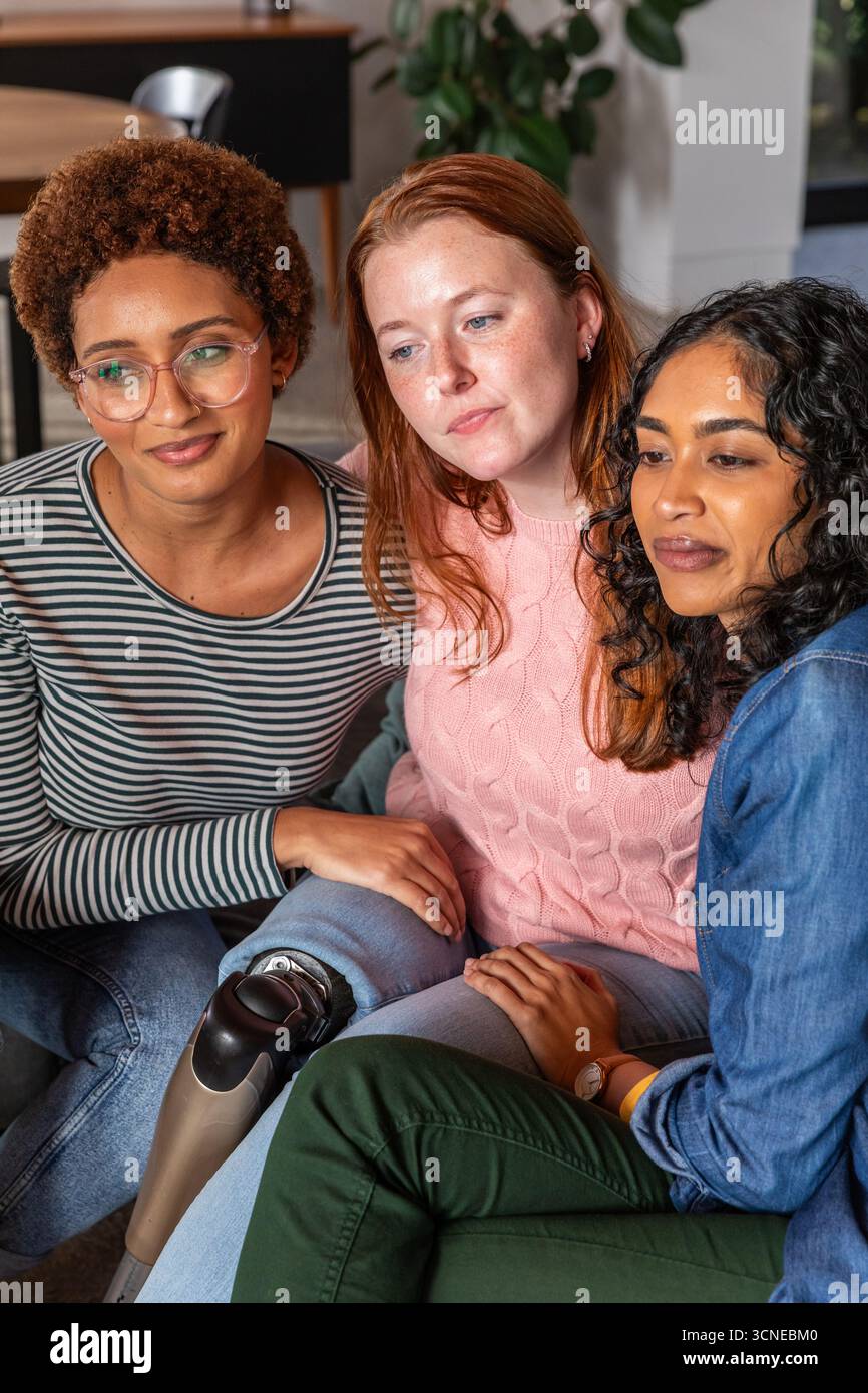 Diverses amies féminines assises sur le canapé à la maison portant des lunettes, mettant en vedette la jambe prothétique Banque D'Images
