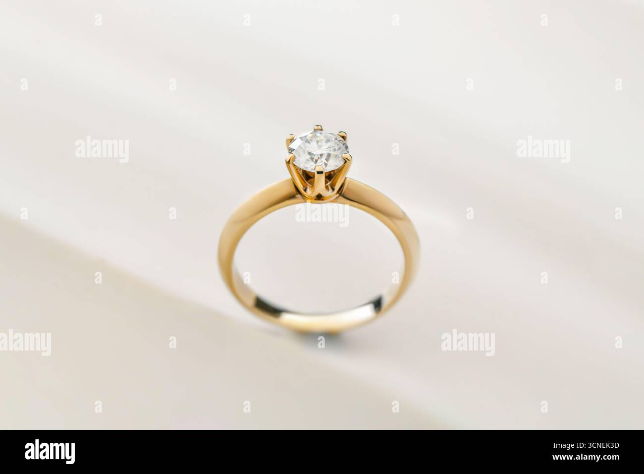 Une belle bague en diamant or et blanc avec un grand diamant au centre. La bague est sertie dans une bande d'or et est placée sur une surface blanche. La bague Banque D'Images