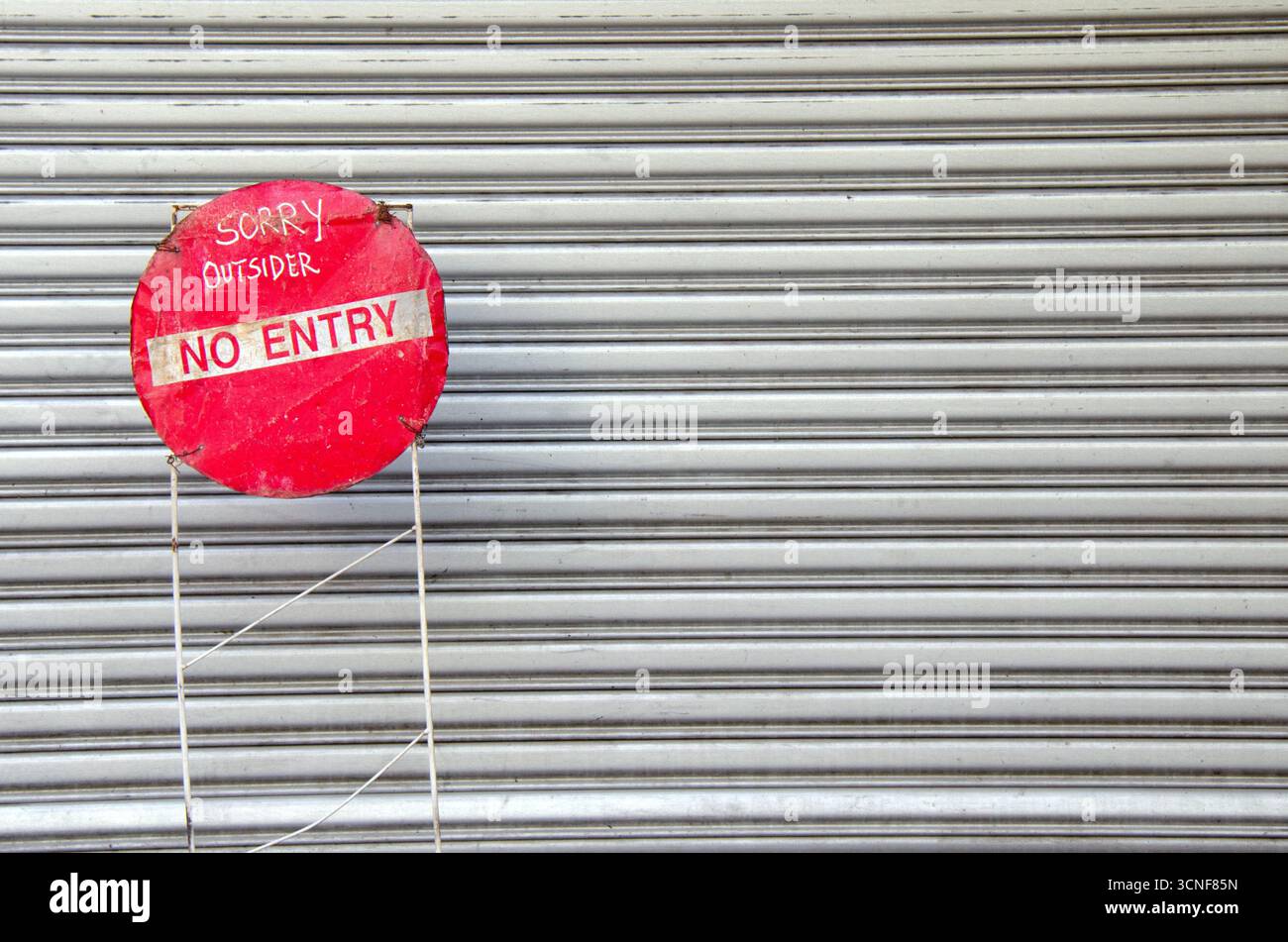 Signe « INTERDICTION D’ENTRÉE » fait à la main avec texte manuscrit sur cadre métallique devant le volet roulant fermé, symbolisant l’accès restreint ou la vie privée. Banque D'Images