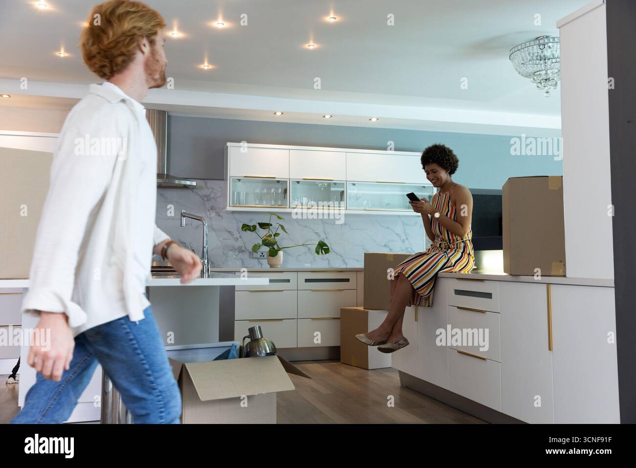 Divers couples déballant des boîtes dans la cuisine, femme vérifiant le smartphone sur le comptoir Banque D'Images