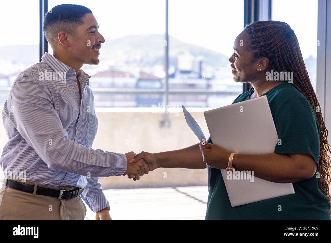 Divers collègues se serrant la main près du mur de verre dans le bureau d'entreprise avec ordinateur portable, dossier Banque D'Images