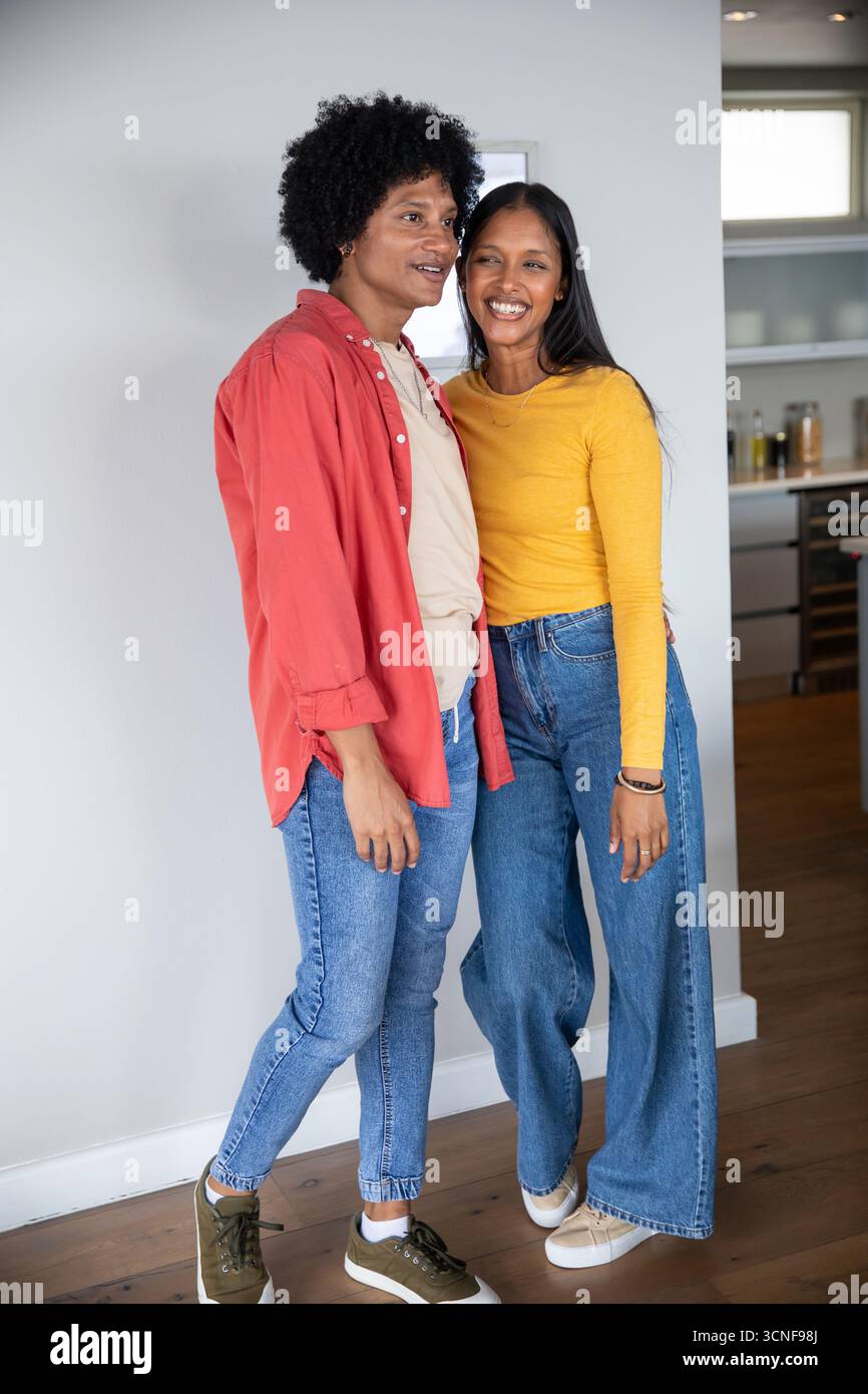 Couple diversifié se penchant l'un vers l'autre et souriant à la caméra dans la cuisine de la maison, pots de comptoir Banque D'Images Couple diversifié se penchant l'un vers l'autre et souriant à la caméra dans la cuisine de la maison, pots de comptoir Banque D'Images