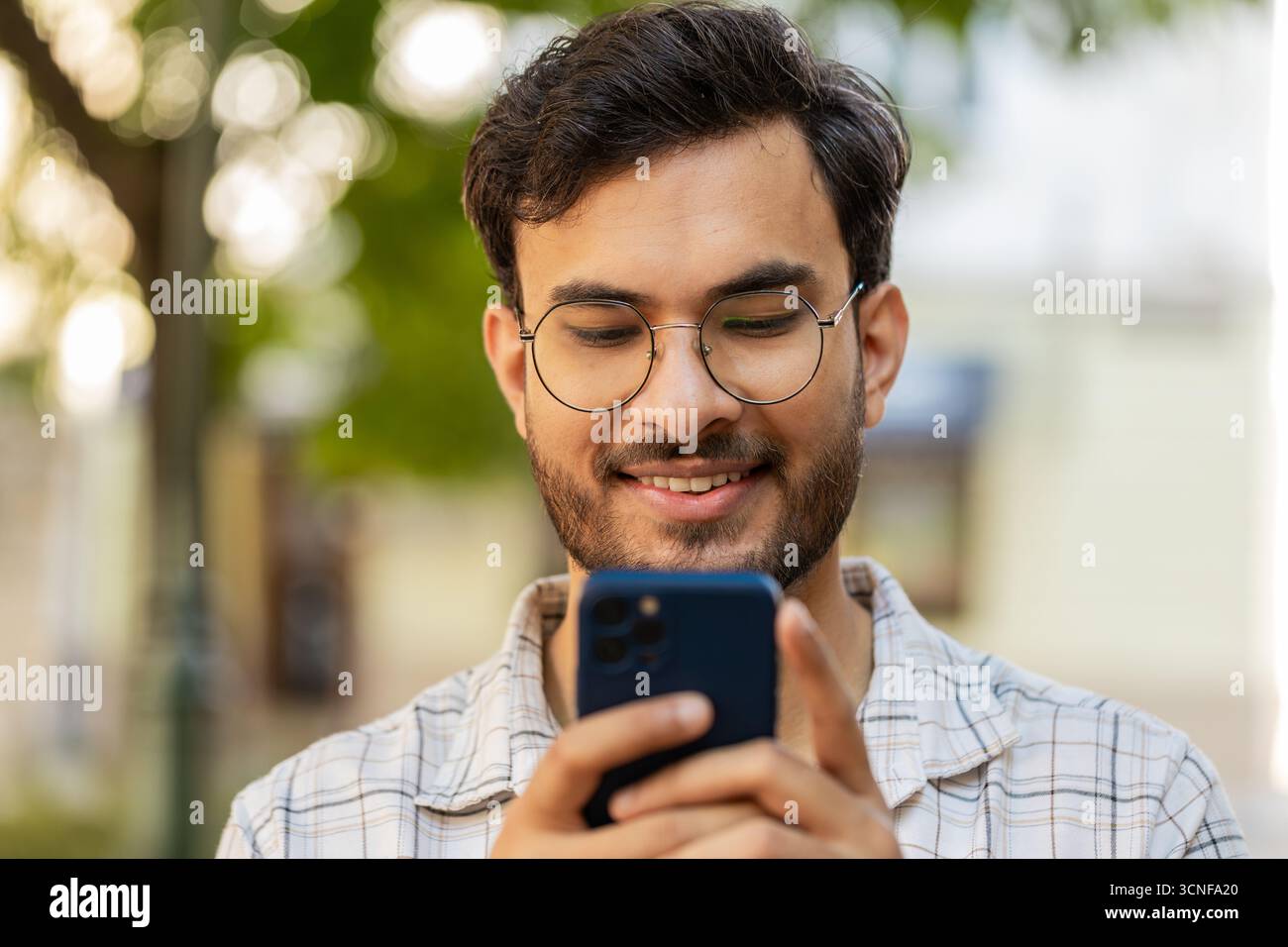 Jeune homme indien utilisant un smartphone tapant des messages texte dans l'application de médias sociaux en ligne, surfant sur Internet, se relaxant, prenant une pause à l'extérieur. Un type hispanique debout sur la rue urbaine. Horizontal Banque D'Images